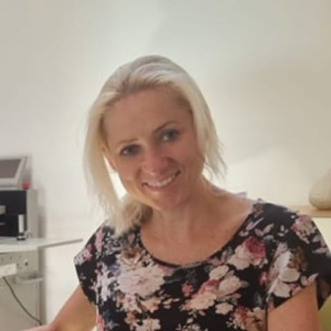 Porträt von Angelika Burgstaller, lächelnd, an ihrem Schreibtisch im Büro.